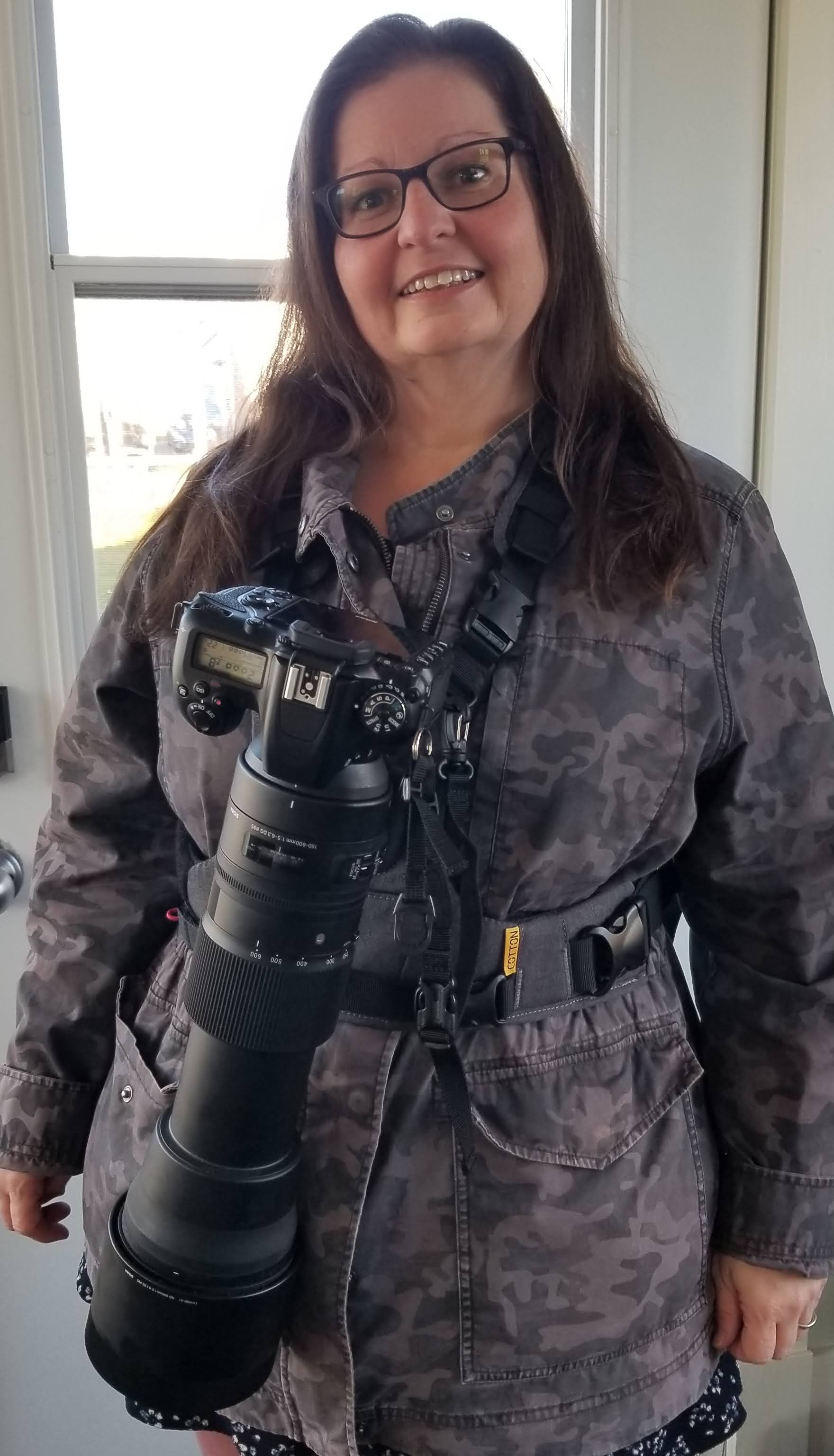 Me wearing a camera harness vest with a large camera and VERY large lense attached, taking up almost the length of my entire upper body.